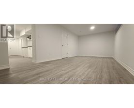 A spacious room with wooden flooring and white walls, labeled as a brokerage by Right at Home Realty.