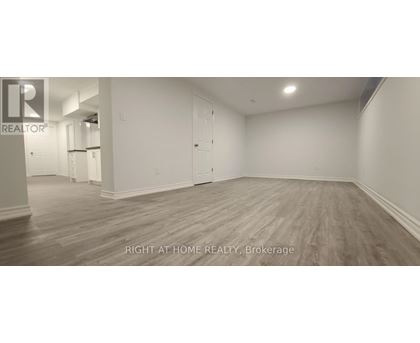 A spacious room with wooden flooring and white walls, labeled as a brokerage by Right at Home Realty.