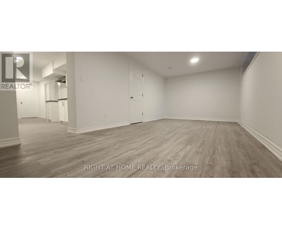 A spacious room with wooden flooring and white walls, labeled as a brokerage by Right at Home Realty.