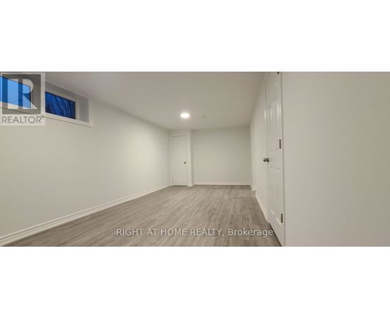 A spacious room with wooden flooring and white walls, with a door on the right side.