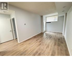 A room with wooden flooring and white walls, with a door on the left and a window with blinds on the right.