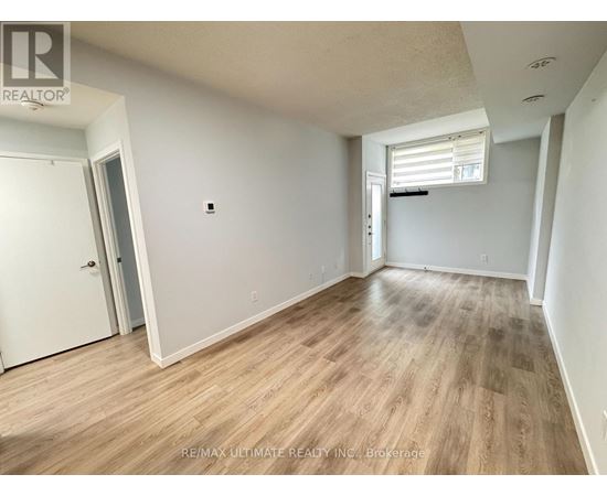A room with wooden flooring and white walls, with a door on the left and a window with blinds on the right.