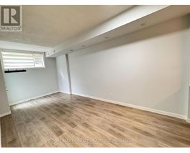 A room with wooden flooring and white walls, with a window on the left side.