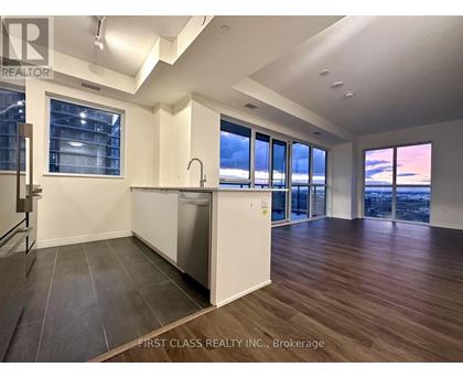 A kitchen with a dishwasher and a refrigerator in a room with wooden floors and a large window.