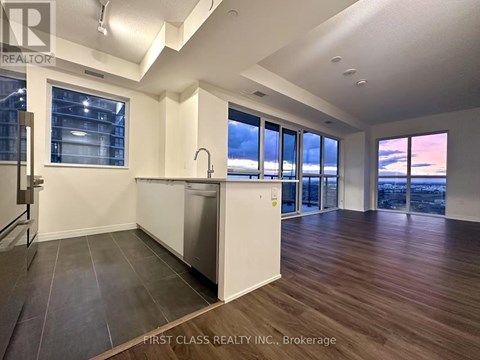 A kitchen with a dishwasher and a refrigerator in a room with wooden floors and a large window.