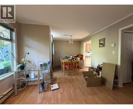 A room with a dining table and chairs in the middle of the room with boxes on the floor.