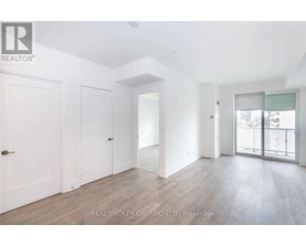 A spacious room with white walls and wooden flooring, featuring a sliding glass door leading to a balcony.