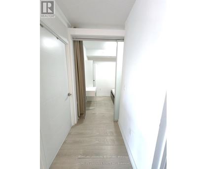 A hallway with a door on the left and a bedroom with a bed and a window on the right.