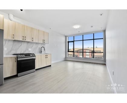A spacious kitchen with wooden cabinets and a large window overlooking a building.