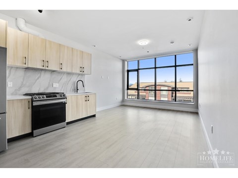 A spacious kitchen with wooden cabinets and a large window overlooking a building.