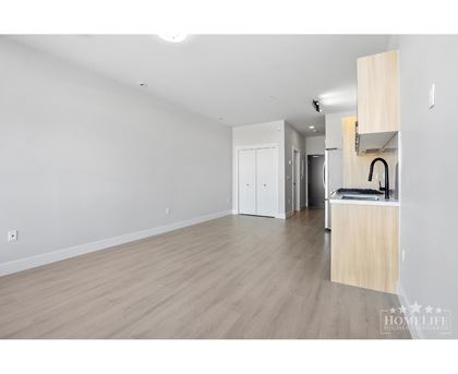 A spacious room with wooden flooring and white walls, featuring a kitchenette with a sink and cabinets.