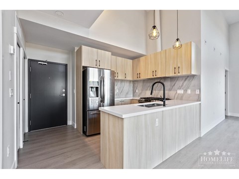 A modern kitchen with a black fridge and wooden cabinets.