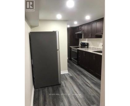 A black refrigerator in a kitchen with wooden floors and white walls.