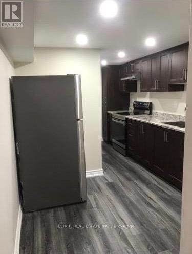 A black refrigerator in a kitchen with wooden floors and white walls.