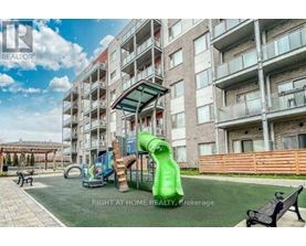 A playground area with a green slide and a wooden fence in front of apartment buildings.