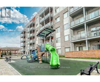 A playground area with a green slide and a wooden fence in front of apartment buildings.