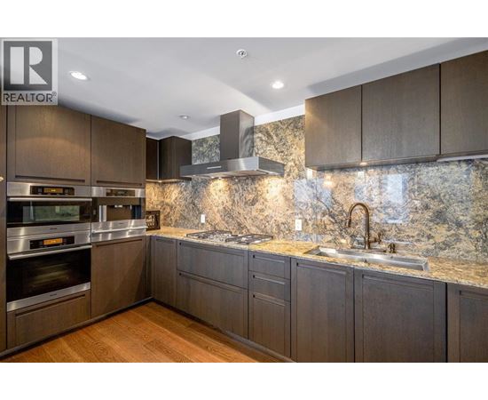 A modern kitchen with dark wood cabinets and a marble backsplash.