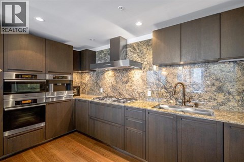 A modern kitchen with dark wood cabinets and a marble backsplash.