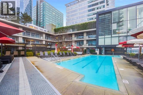 A large swimming pool in a city setting with a red umbrella.