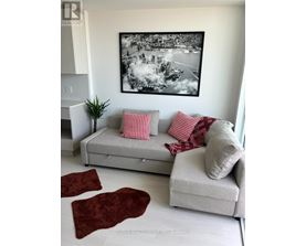 A living room with a grey couch, red pillows, and a large black and white picture on the wall.