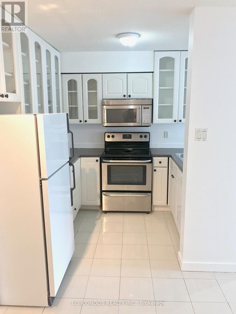 A white kitchen with a refrigerator on the left and a stove top oven in the middle.