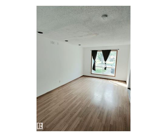 A room with wooden flooring and a window with a view of a street.
