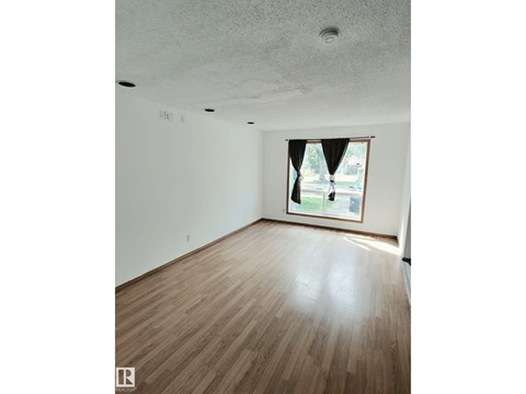 A room with wooden flooring and a window with a view of a street.