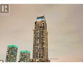 A tall building with a glass facade stands in front of two shorter buildings.