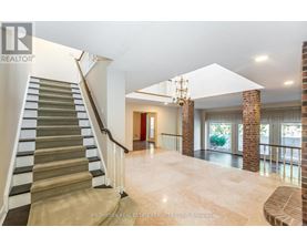 A spacious living room with a staircase on the left side and a chandelier hanging from the ceiling.