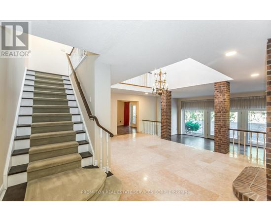 A spacious living room with a staircase on the left side and a chandelier hanging from the ceiling.