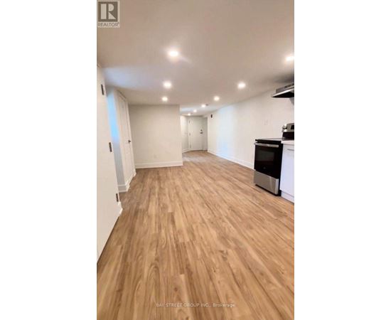 A spacious room with wooden flooring and a kitchen area with a stove and oven.