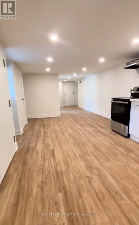 A spacious room with wooden flooring and a kitchen area with a stove and oven.