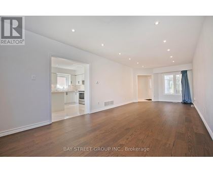 A spacious room with wooden floors and white walls, with a view into another room through a glass door.
