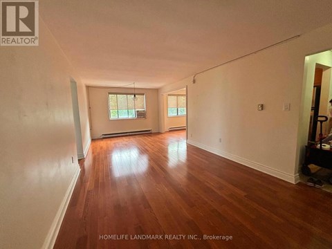 A room with wooden floors and white walls, with a window and a door visible.