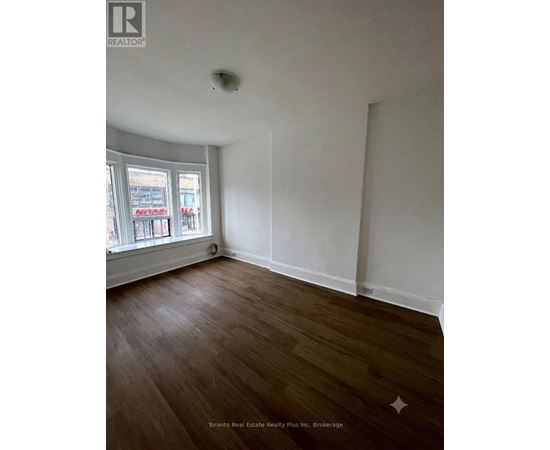 A room with wood flooring and a window showing a street view.