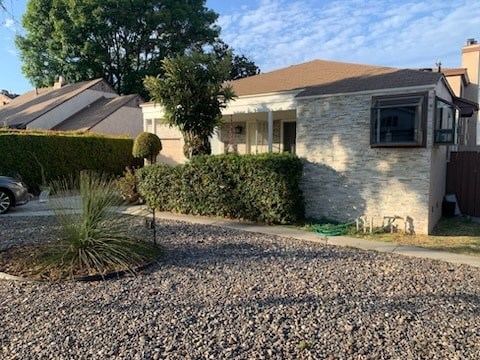 A house with a brown roof and a grey stone wall with a green bush in front.