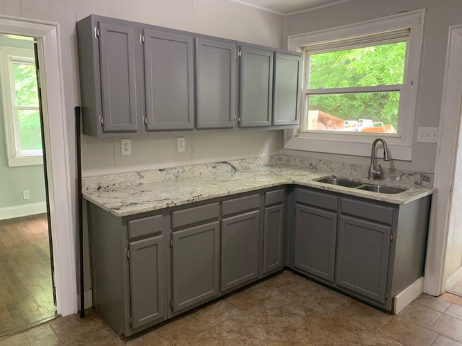 A kitchen with grey cabinets and a marble countertop.