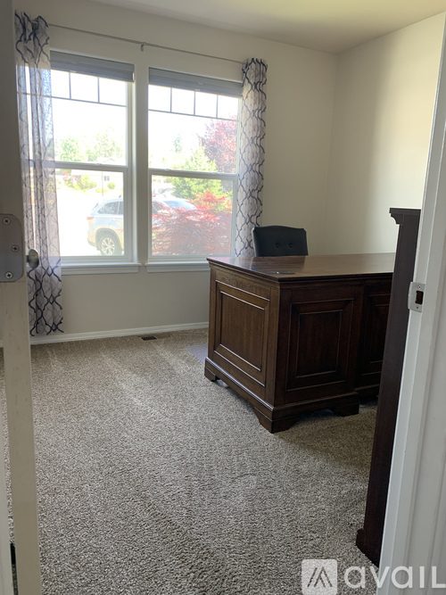 A room with a desk and a window with a view of a car and trees.