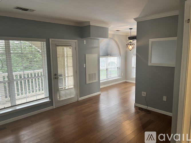 A spacious room with wooden floors and a large window with blinds.
