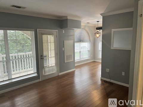 A spacious room with wooden floors and a large window with blinds.
