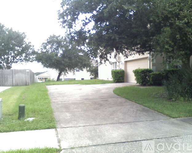 A driveway leads to a house with a fence and trees.