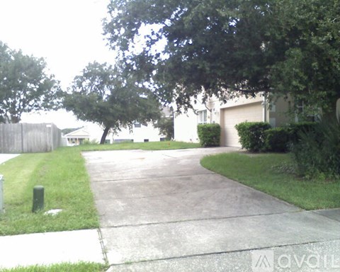 A driveway leads to a house with a fence and trees.