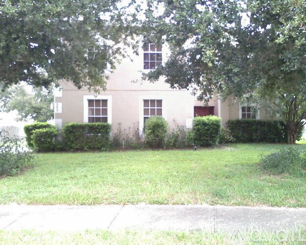 A white building with a red door and windows is surrounded by greenery.