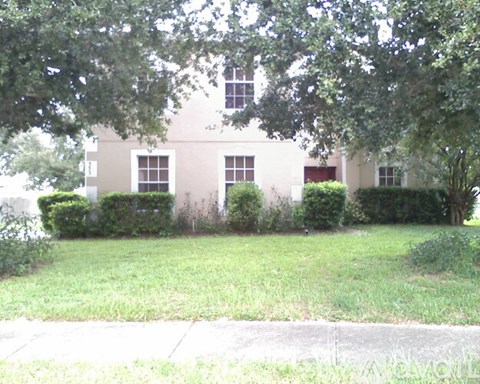 A white building with a red door and windows is surrounded by greenery.