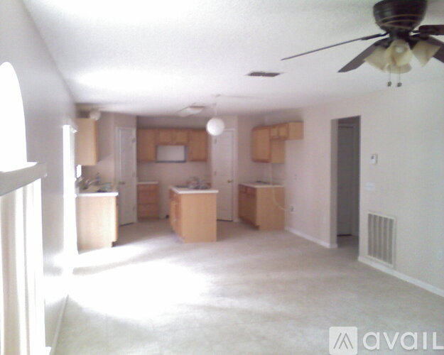 A living room with a ceiling fan and a kitchen area in the background.