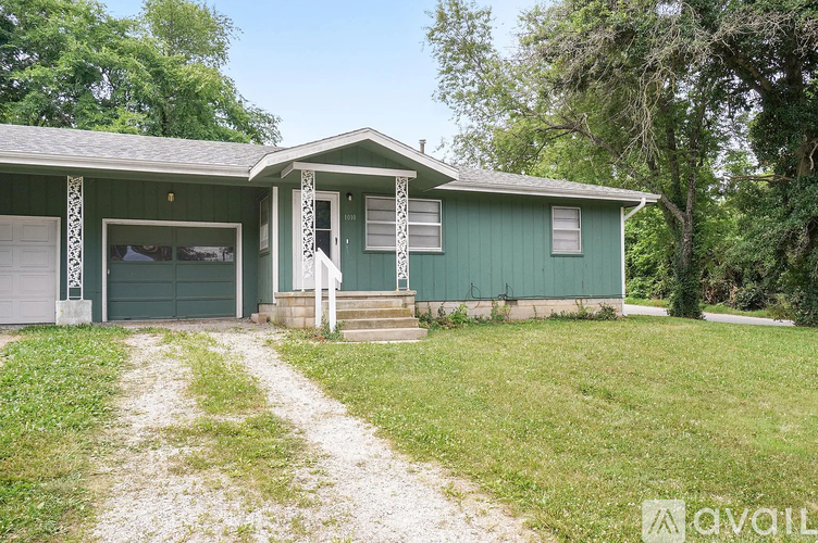 A green house with a white porch and a gravel driveway.