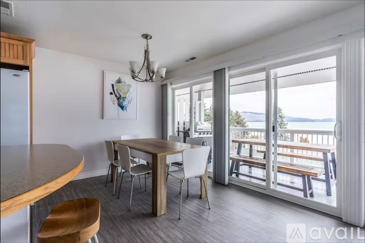 A dining area with a wooden table and chairs, a chandelier, and a view of the outdoors through a sliding glass door.