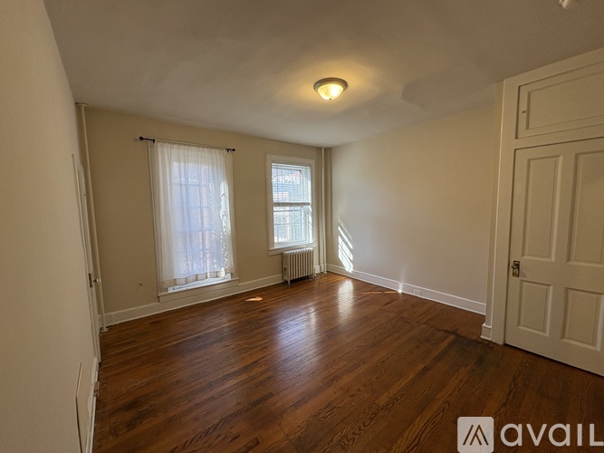 A room with wooden floors and white walls, with a window and a door.