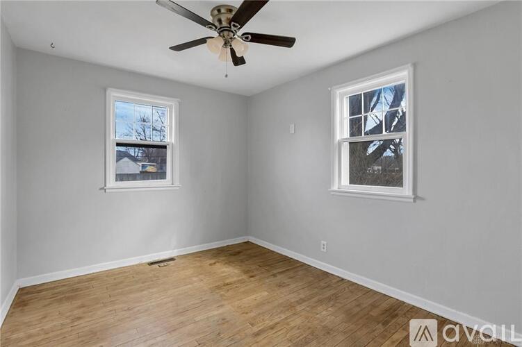 A room with a ceiling fan and two windows.