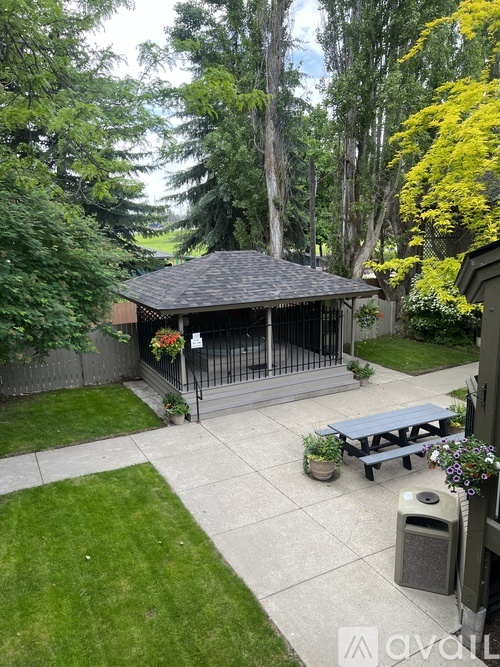 A backyard with a pavilion, picnic table, and a trash can.